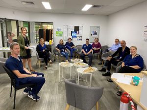 A group of people sit in a half circle. Many of them are wearing scrubs.