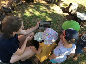 A young woman holds a phone up to small children. 