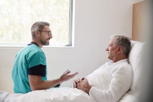 Surgeon Visiting And Talking With Senior Male Patient In Hospital Bed In Geriatric Unit